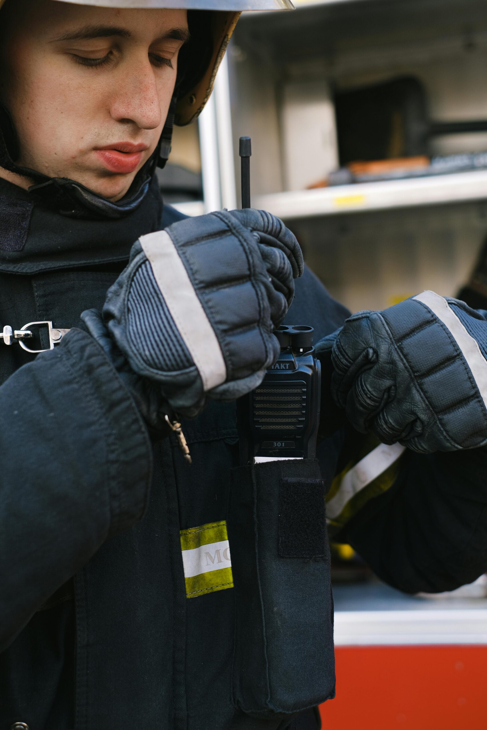 Close-up of a firefighter in turnout gear adjusting a walkie talkie on duty.